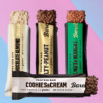 Een reeks van vier Barebells eiwitrepen in diverse smaken, waaronder Cookies & Cream, Chocolate Almond, Salty Peanut, en Mint & Nougat, getoond tegen een kleurrijke roze en blauwe diagonale achtergrond.