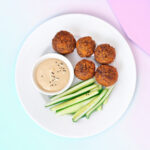 Banner van Keto falafel balletjes geserveerd met een frisse komkommersalade en tahinisaus, gepresenteerd op een wit bord tegen een achtergrond van zachte pastelkleuren.